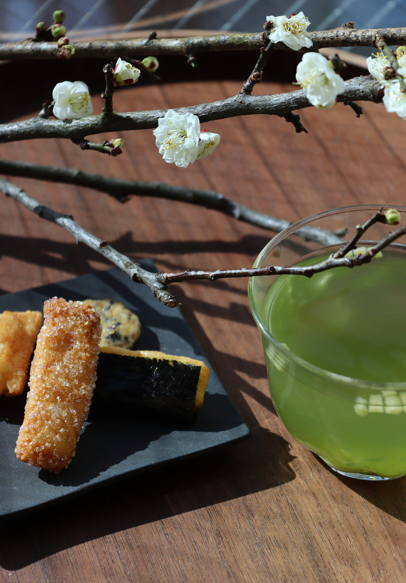 ume kombucha and Japanese rice crackers on a table next to plum blossoms